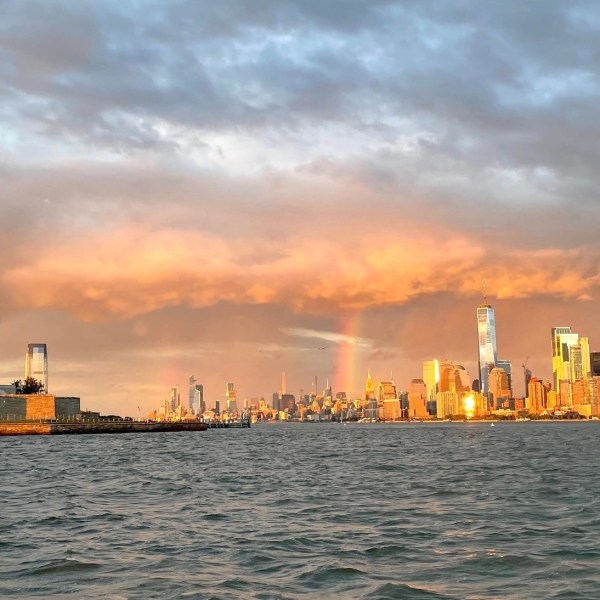 statue of liberty during a new york sunset cruise with city skyline and rainbow in background