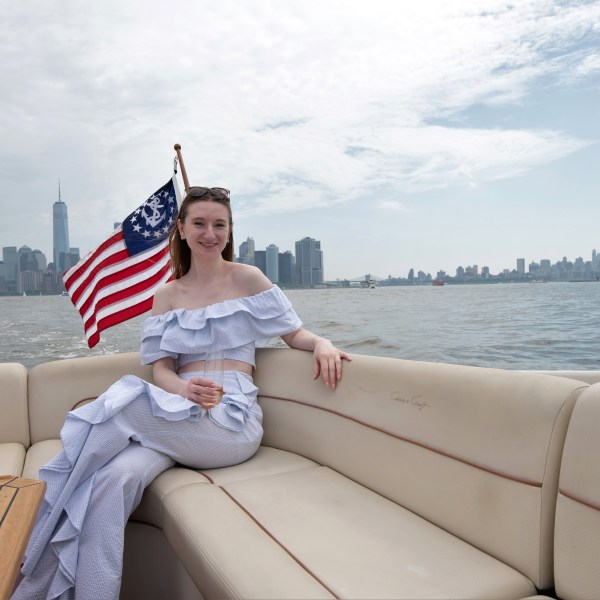 woman drinking champagne on a boat charter in NYC with the flag behind her