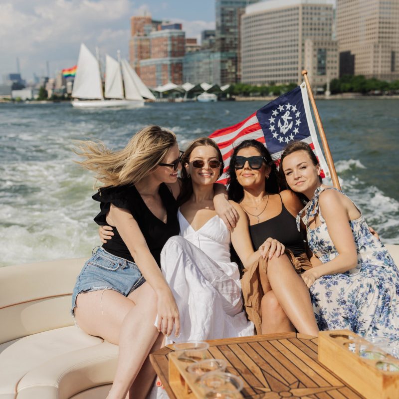 a group of friends on a boat rental NYC party with a sailboat and the financial district in the background