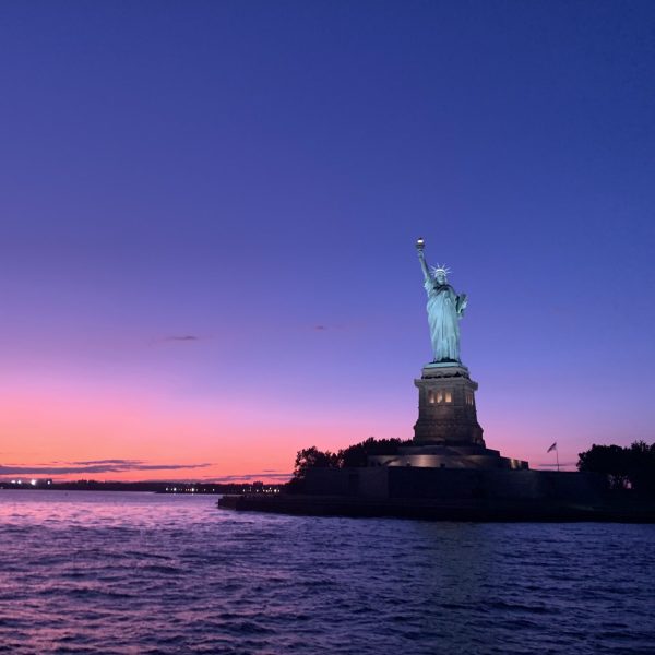 pink and purple sky behind the Statue of Liberty during a private sunset cruise NYC