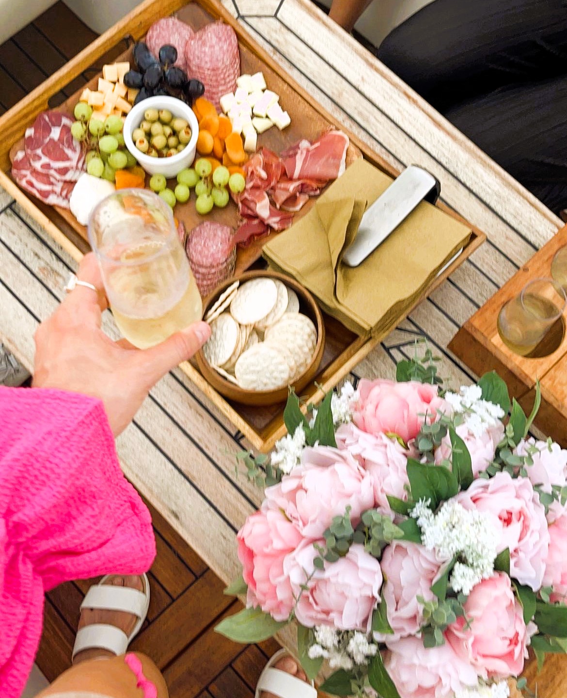 hand with pink ruffles grabbing a champagne flute with charcuterie board and pink flowers makes how much to rent a boat in nyc a priceless event