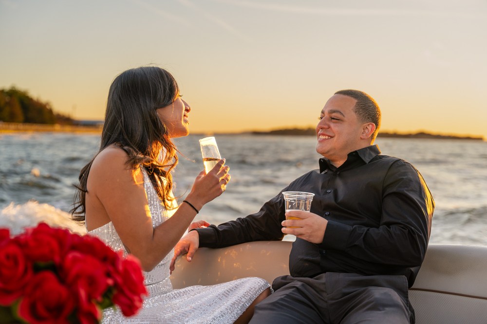 Couple enjoys drinks on a private boat ride at sunset, with red roses in the foreground.