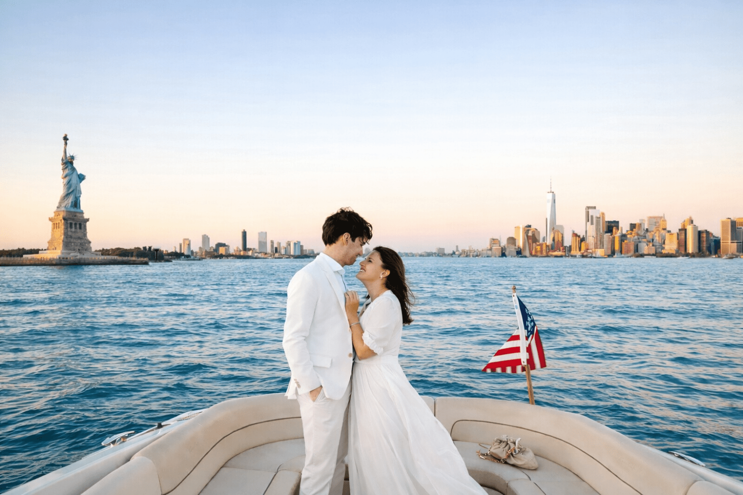 Couple in white on a yacht during a wedding in the New York Harbor near the Statue of Liberty, NYC skyline in the background.