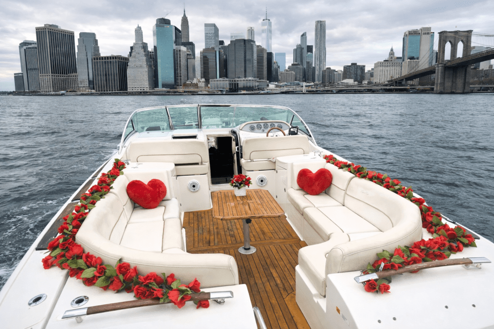 Private yacht with red flowers and heart cushions on deck, with the NYC financial district skyline in the background.