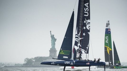Catamarans from the USA and AUS race near the Statue of Liberty on a foggy day during the Mubadala Sail Grand Prix in New York, viewed from a yacht.