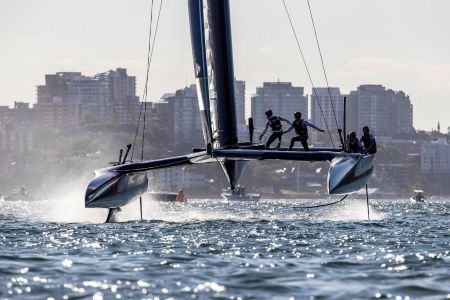 Catamaran with crew foiling on water during the SailGP New York, city skyline in background, viewed from a private boat.
