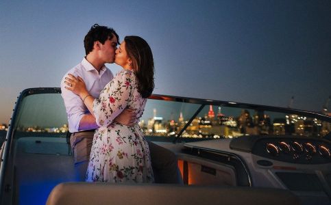 Couple kisses on a boat at night with city skyline in the background.