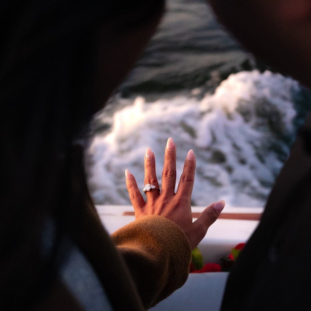 Close-up of a hand with an engagement ring on a boat during a marriage proposal, with water in the background.