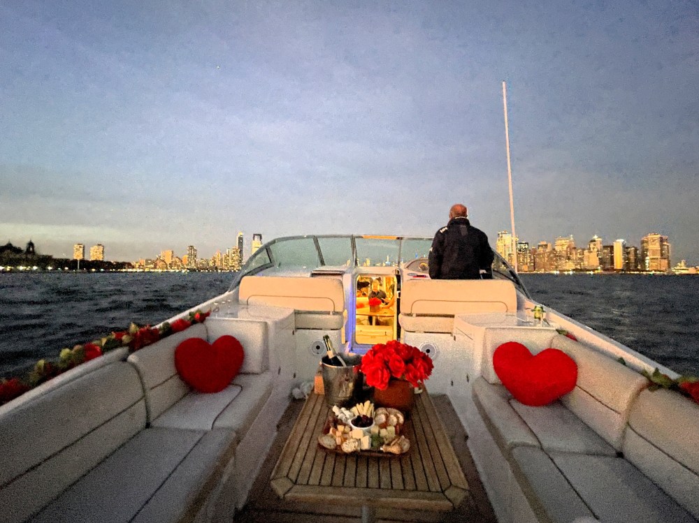 Private boat cruise at sunset with heart-shaped pillows on deck and the NYC skyline in the background.