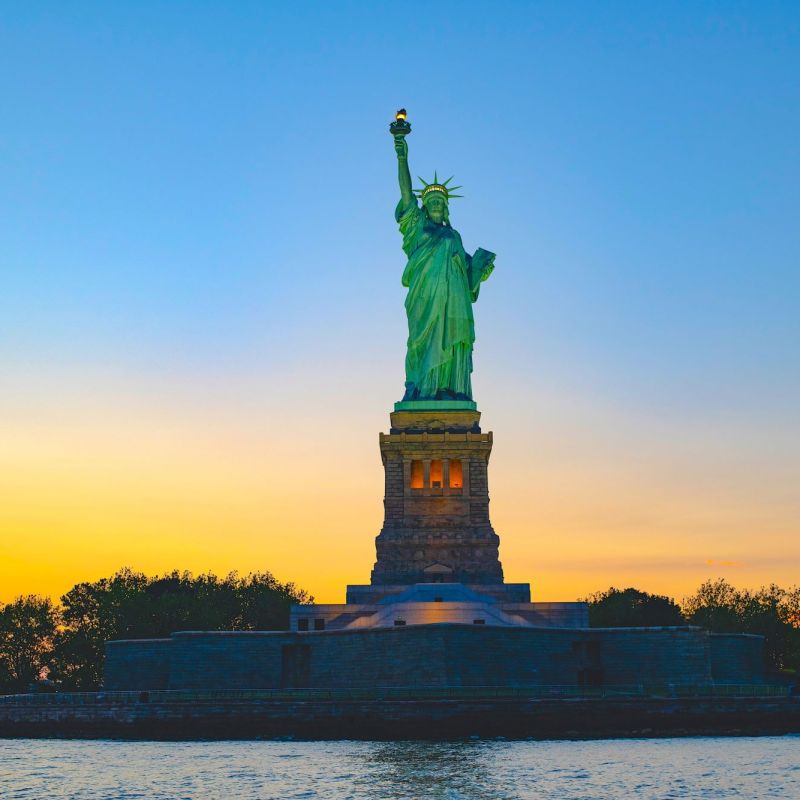 Statue of Liberty at sunset with a colorful sky in the background during a private boat tour of NYC.