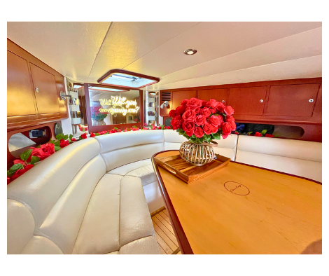 Boat cabin interior with white seating, red roses, and 'Will you marry me?' sign for a proposal in NYC.