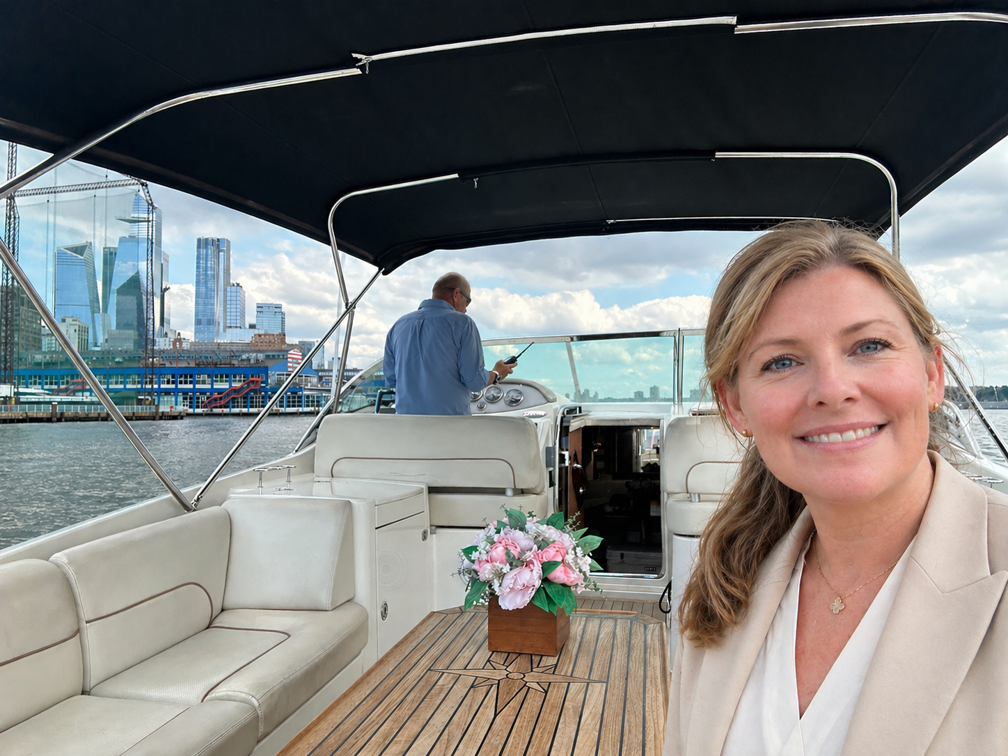 Smiling woman on a private boat tour in NYC with city skyline and captain steering.