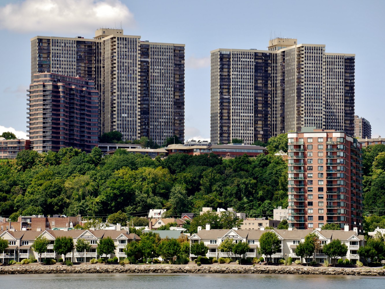 Tall buildings on a hill behind smaller houses near water.