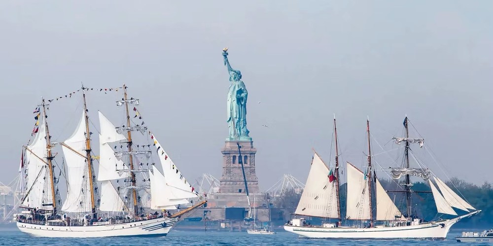 Two sailing ships near the Statue of Liberty on a clear day.