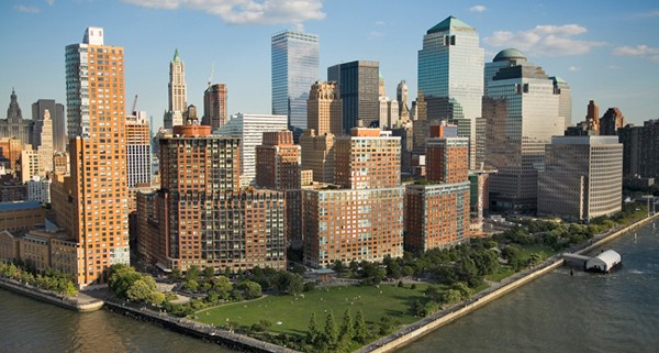 Skyline of a city with tall buildings and a riverside park.