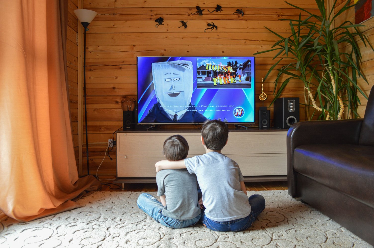 Two kids watch a cartoon on TV in a cozy wooden room.