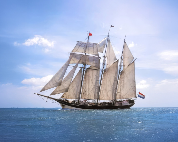 Sailing ship with multiple sails on open sea under blue sky.
